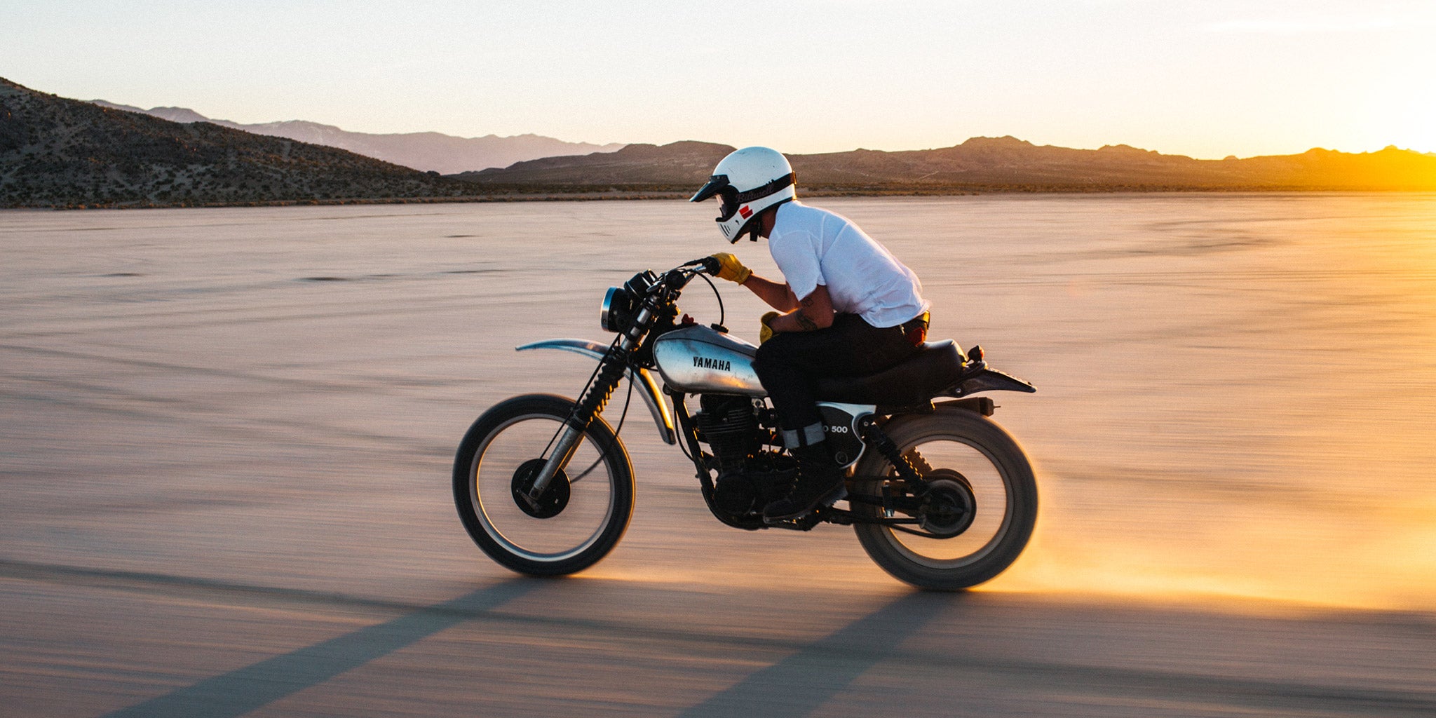 夕方の乾いた湖の上を、YAMAHA のオートバイで走るライダー
